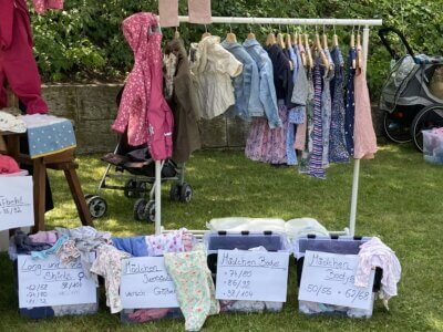 Kleiderständer bei einem Kinderflohmarkt, unten Boxen mit Kleidergrößen