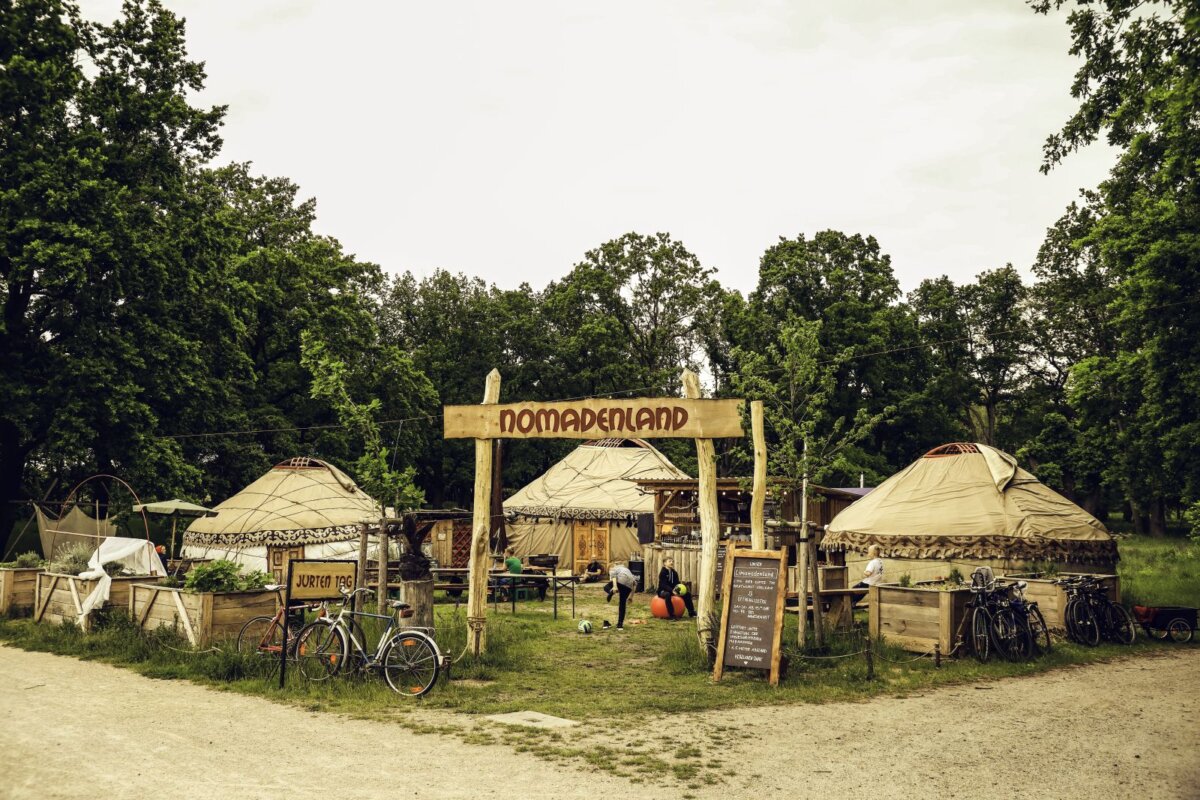 Blick auf Jurtendorf mit drei Jurten und Eingangsbogen mit Schriftzug Nomadenland im Volkspark Potsdam