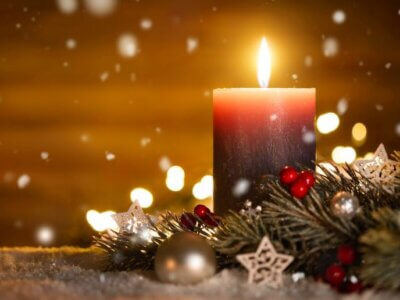 Eine brennende Kerze steht auf einem weihnachtlich gedeckten Tisch